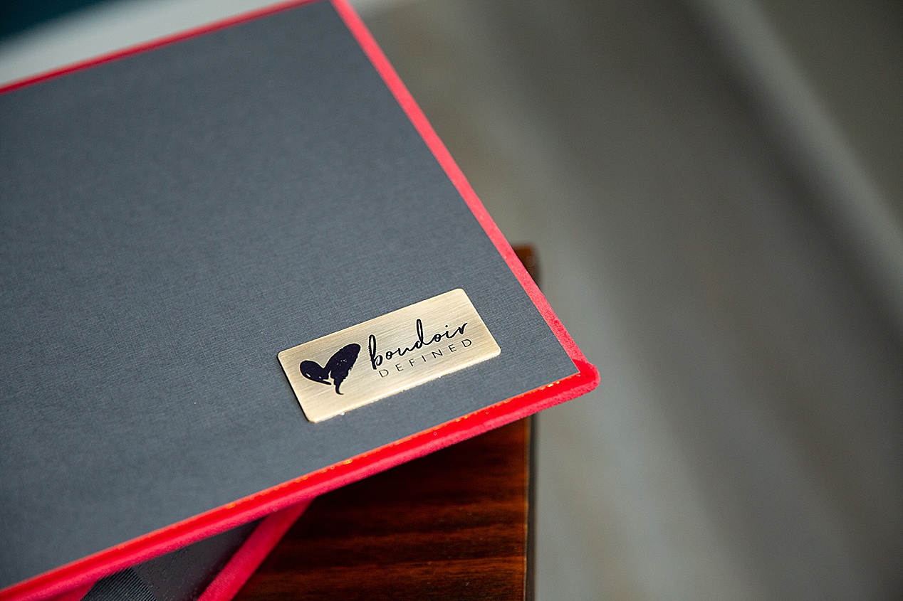 A red velvet boudoir album with the metallic plate reading "Boudoir Defined" out of Meridian, Idaho.
