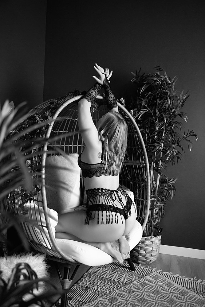 Black and white photo of woman posing showing butt on Egg Chair in Boudoir Defined Boudoir Photography Studio in Boise, Idaho.