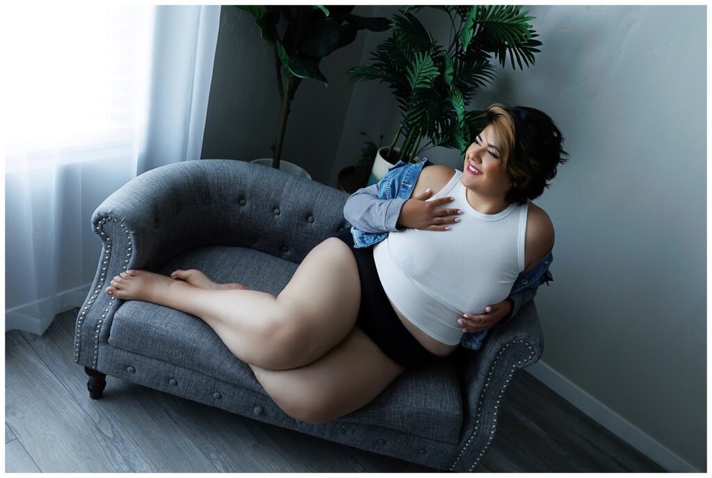 Plus sized Hispanic woman in jean jacket and white tank top looking casually outside in Boise Idaho's Boudoir Defined's Photography Studio.
